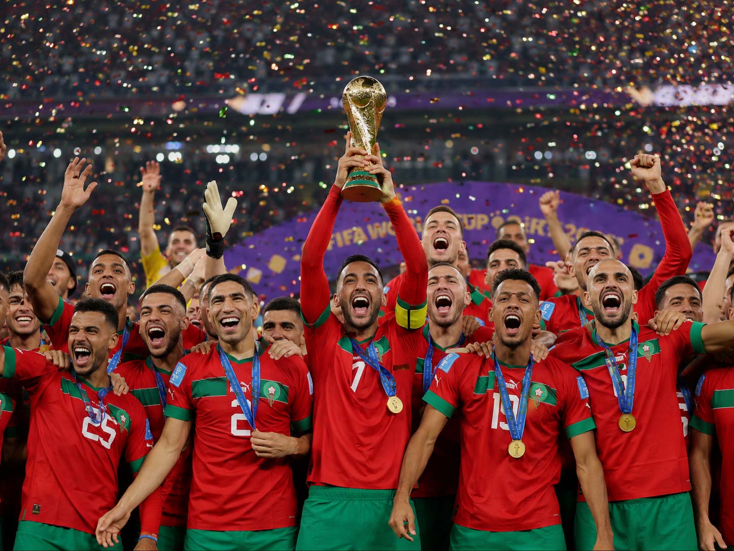 Équipe du Maroc célébrant une victoire en Coupe du Monde 2026, joueurs en maillot rouge soulevant le trophée dans un stade sous les confettis